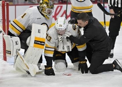 Boston Bruins defenseman Charlie McAvoy (73) is tended by a trainer and teammate goalie Jeremy Swayman (1) after receiving a shot in the mouth during the second period of the game against the Montreal Canadiens at the Bell Centre.