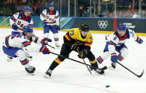 Lukas Reichel of Germany in action with Zach Werenski of United States and Jake Sanderson of United States in men's ice hockey group C play during the Milano Cortina 2026 Olympic Winter Games at Milano Santagiulia Ice Hockey Arena.