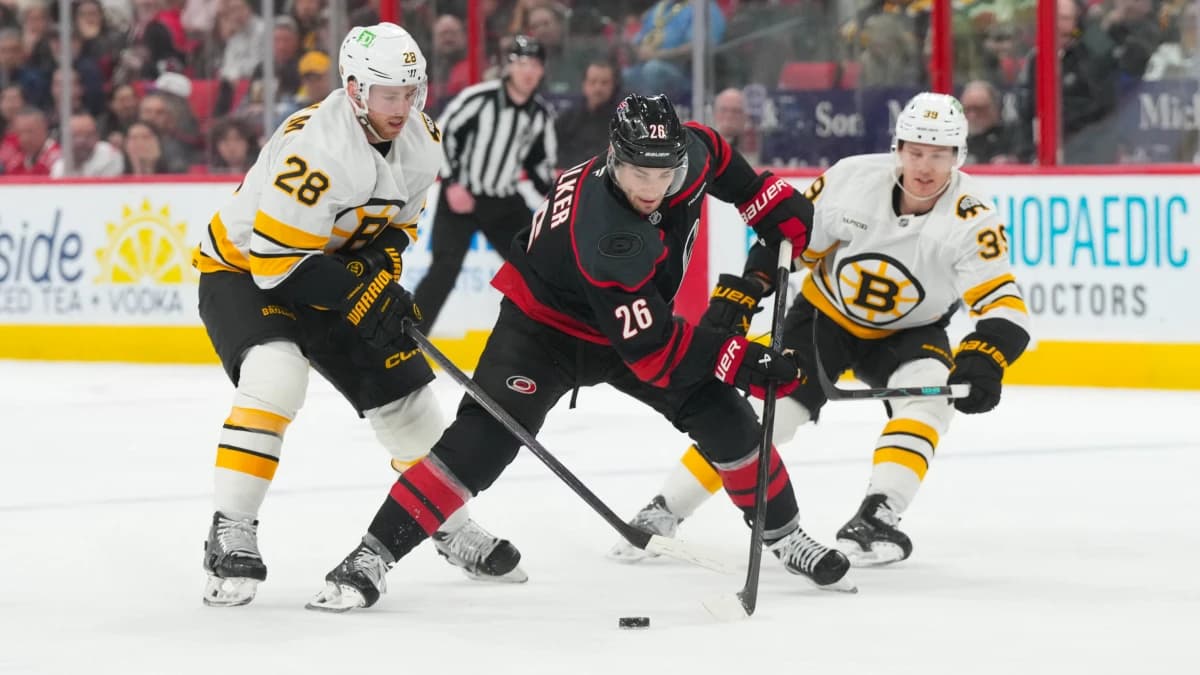 Carolina Hurricanes defenseman Sean Walker (26) skates with the puck between Boston Bruins center Elias Lindholm (28) and center Morgan Geekie (39) during the third period at Lenovo Center.