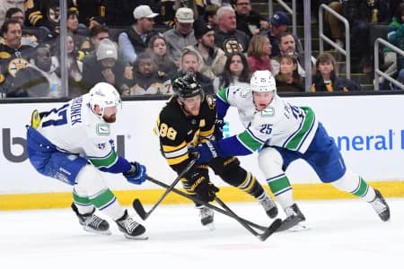 Boston Bruins right wing David Pastrnak (88) passes the puck between Vancouver Canucks defenseman Filip Hronek (17) and defenseman Elias Pettersson (25) during the third period at TD Garden.